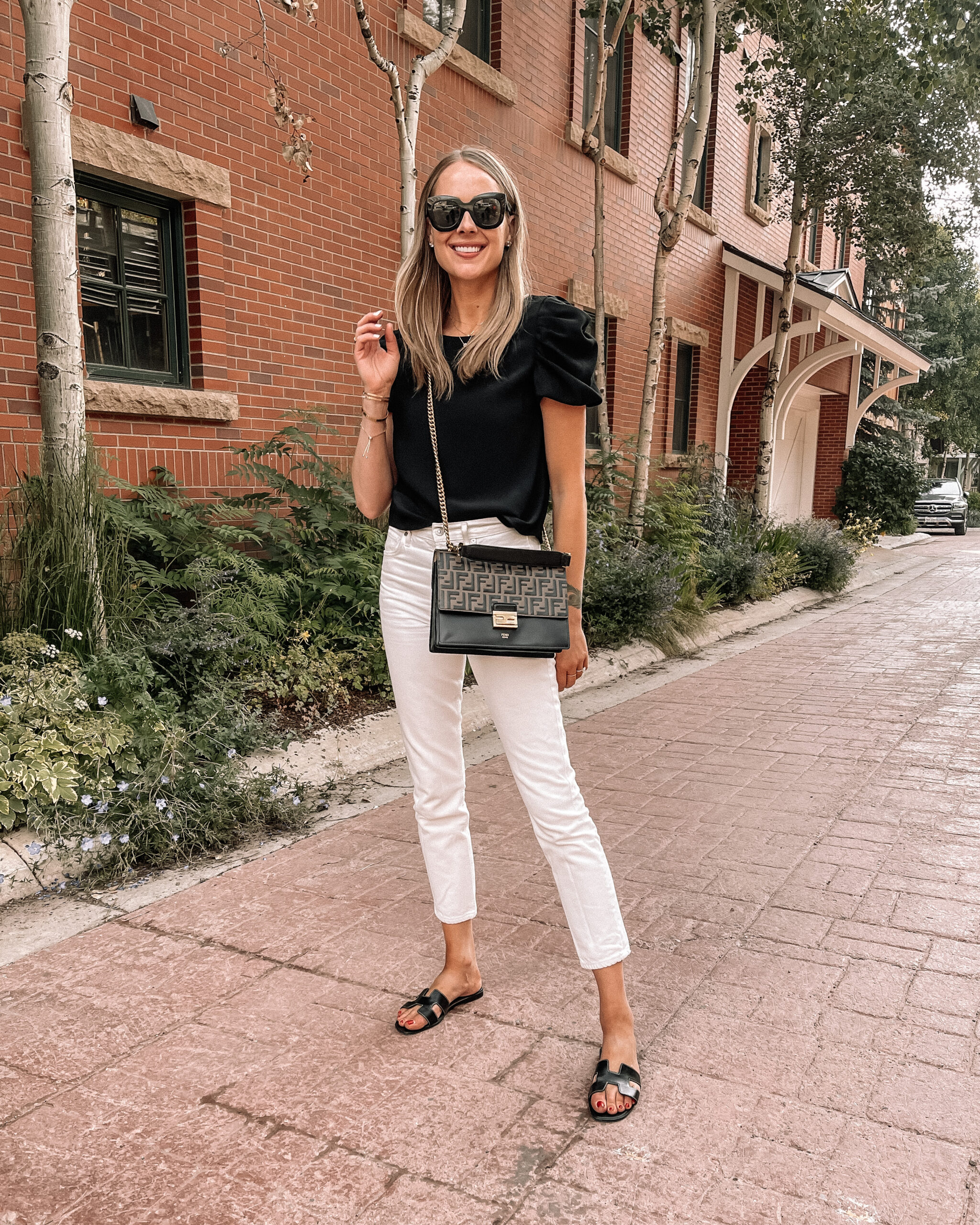 Fashion Jackson Wearing Amanda Uprichard Black Puff Sleeve Top Citizens of Humanity White Jeans Hermes Oran Black Sandals Telluride Summer Outfit